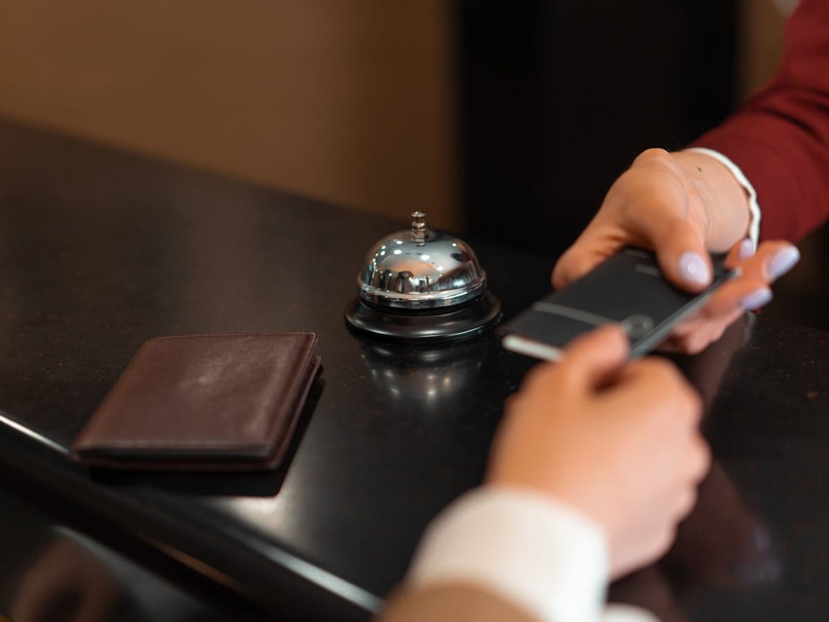 A guest handing over a phone at a hotel front desk with a service bell